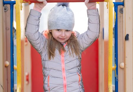 Pretty kid girl on the playground hanging on the bar