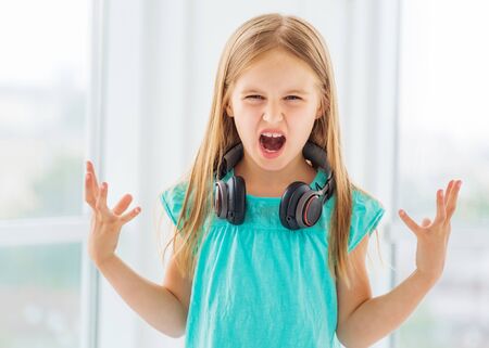 Active small girl with headphone sand hands up is singing loudly with perfect talentの写真素材