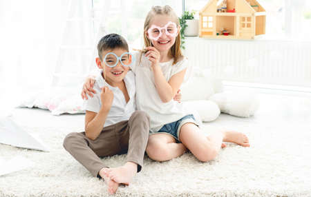 Portrait of cute little girl and boy wearing paper glasses in kids roomの写真素材