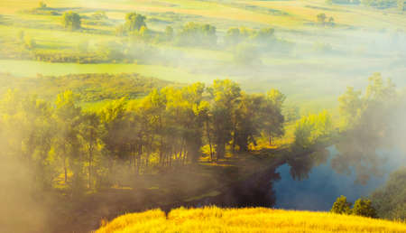 Foggy morning above picturesque river and fieldの写真素材