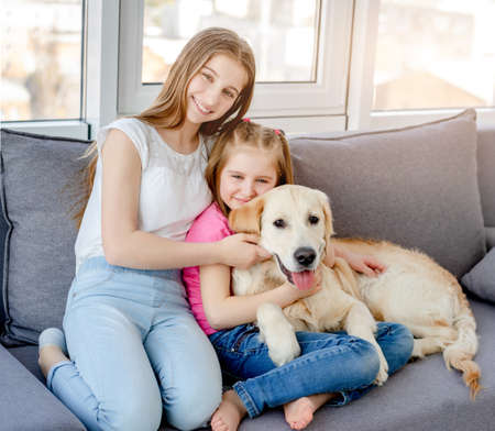 Smiling girls cuddling lovely dog in light roomの写真素材
