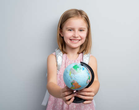 Schoolgirl holding small globe in front of her on gray backgroundの写真素材