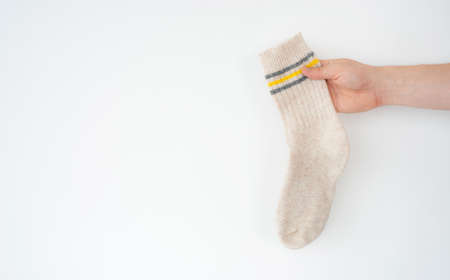 Beige woolen sock in hand on light background