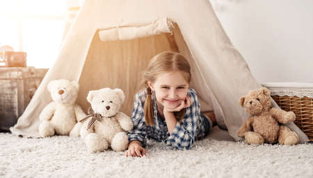 Smiling little girl lying in wigwam with teddy bears, panoramic orientationの写真素材