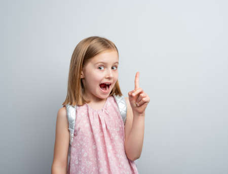 Little girl with school backpack pointing finger up, idea concept