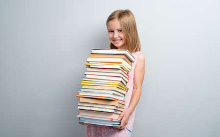 Smiling school girl holding stack of books on a grey wall backgroundの写真素材