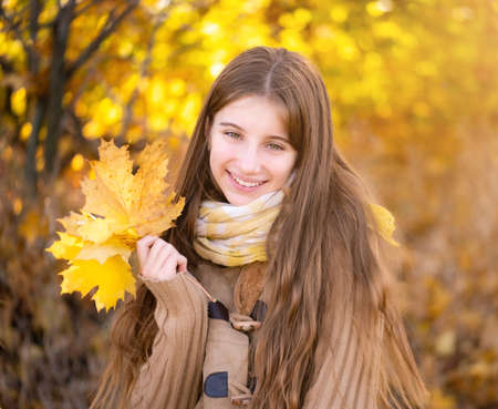 Smiling teenage girl holding yellow leaves in parkの写真素材
