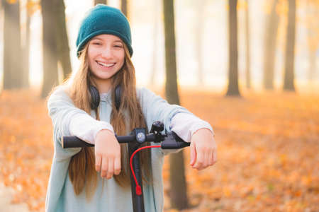 Lovely teenage girl with scooter resting in autumn parkの写真素材