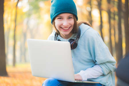 Smiling teenage girl sitting on bench with laptopの写真素材