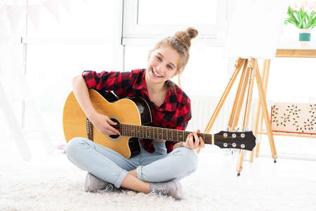 Happy teenage girl playing guitar in bright roomの写真素材