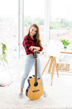 Happy teenage girl with guitar in bright roomの写真素材