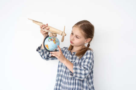 Cute little girl flying wooden plane over globe on white wall backgroundの写真素材