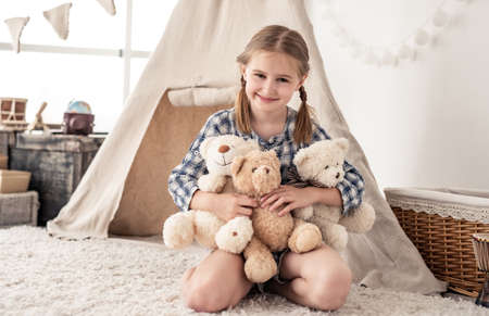 Happy little girl hugging plush bears on wigwam backgroundの写真素材