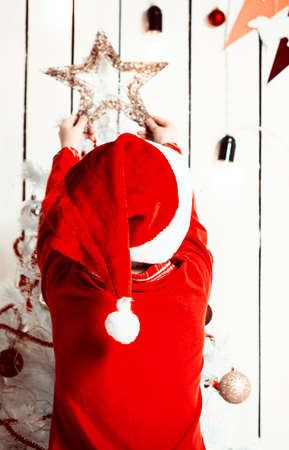 little girl in red hat putting a star on top of christmas tree in decorated roomの写真素材