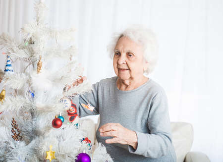 Smiling senior woman decorating fancy christmas treeの写真素材