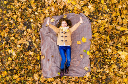 Cute teenage girl lying on back on yellow leaves, view from droneの写真素材
