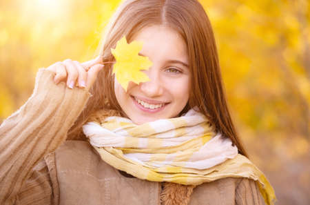 Portrait of happy girl with yellow leaf on autumn background