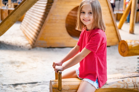Happy little girl riding wooden swing on kids playgroundの写真素材