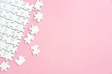 White jigsaw puzzle pieces in corner on pink background with copyspaceの写真素材