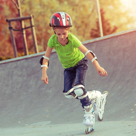 Little girl on roller skates in helmet at a park at sunsetの写真素材
