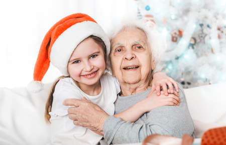 smiling granddaughter in santa hat hugging with grandma at Christmas