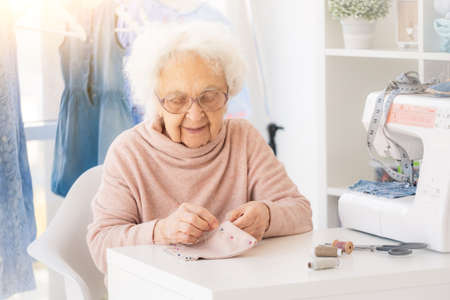 Nice elderly woman sewing in atelier