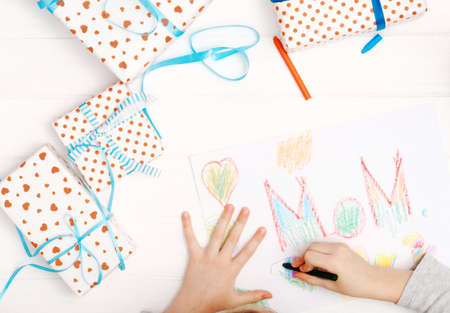 Little girl drawing happy mothers day greeting card with presents on the table
