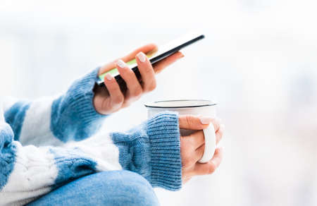 Cup and smartphone in female hands close upの写真素材
