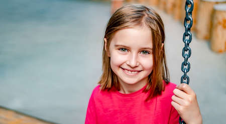 Little girl sitting on chain swing at playground