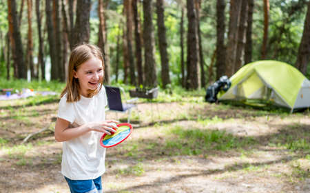 Little girl playing in the camping in the wood with green tent on background. Beautiful smiling kid having activities in the forest with sun lightの写真素材