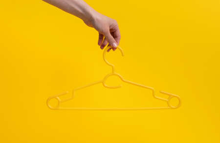 Hand holding hanger isolated on yellow horizontal background with copyspace. Stylish casual design look on fashion accessory. Concept of clothes retailの写真素材