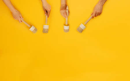 For hands holding paint brushes on yellow background with copy space. Concept of creativity,...
