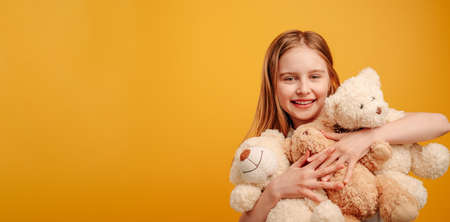 Beautiful girl child with three teddy bears in her hands isolated on yellow background with...