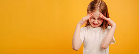Beautiful little girl thinking and holding her hands on her head isolated on yellow background with...