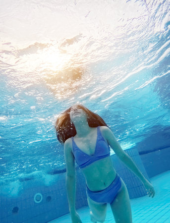 Teen girl swimming under water in blue poolの写真素材