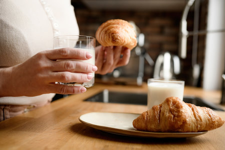 Girl has a breakfast with milk and croissants at kitchenの写真素材