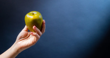 Hand holding green apple on blue background. Organic natural fresh fruit for vegan diet