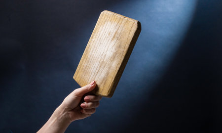 Hand holding toy wooden board for cooking. Craft kitchenware for food preparing on blue backgroundの写真素材