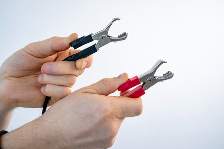 Hands holding crocodile alligator clips red and black color for electrical and electronic testing connect solder. Person measuring of tension and voltageの写真素材