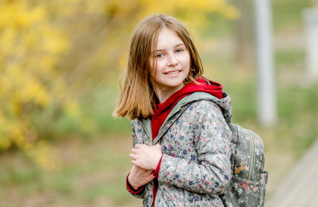 Portrait of beautiful little schoolgirl wth backpack in autumn park