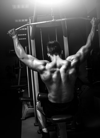 Strong man pulling a vertical upper block, doing back exercises in a modern gym