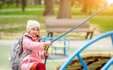 School girl with backpack playing at playground at autumn park. Pretty child kid having fun outdoors after lessonsの写真素材