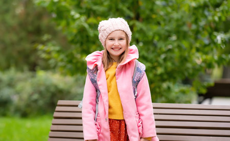 Pretty school girl kid with backpack smiling at autumn park. Beautiful female child portrait with blurred backgroundの写真素材