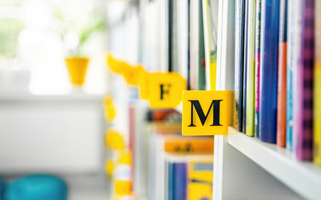 Books on shelves in the light modern school library. Authors of books placed by alphabet.の写真素材