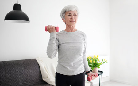 Elderly Woman With Grey Hair, Attractive And Active, Doing Fitness Exercises With Dumbbells At Homeの写真素材