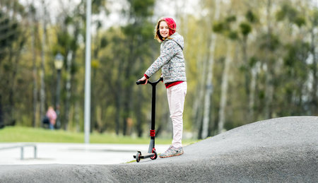 Beautiful little girl rides a scooter in a extreme ride park, smilling and looking into the cameraの写真素材