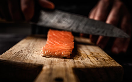 Chief hands cut salmon fillet with knife on wooden table closeup view. Red fish steak for healthy seafood dinnerの写真素材
