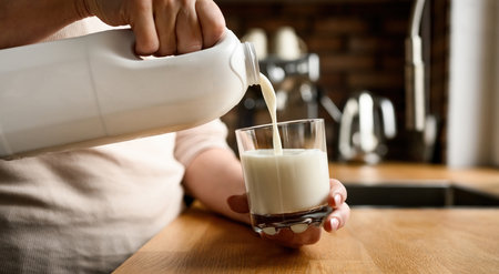 Pouring milk in glass at kitchen at homeの写真素材
