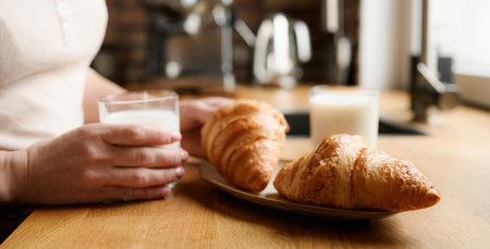 Girl has a breakfast with milk and croissants at kitchen. Woman with white organic latte and french...