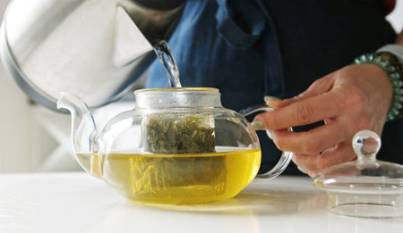 Girl In The Kitchen Filling A Teapot With Hot Water From A Kettle For Green Teaの写真素材